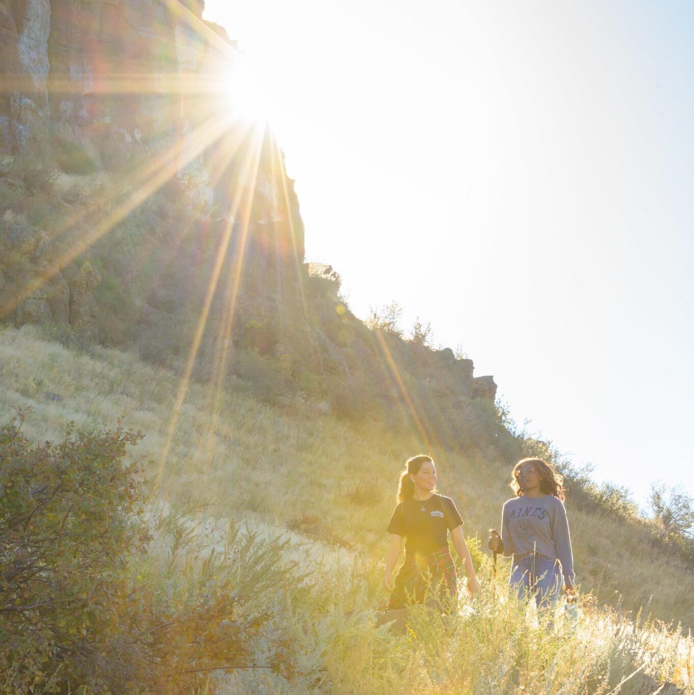 Two Mines students hiking on Mount Zion with sun peeking behind mountain in the background.
