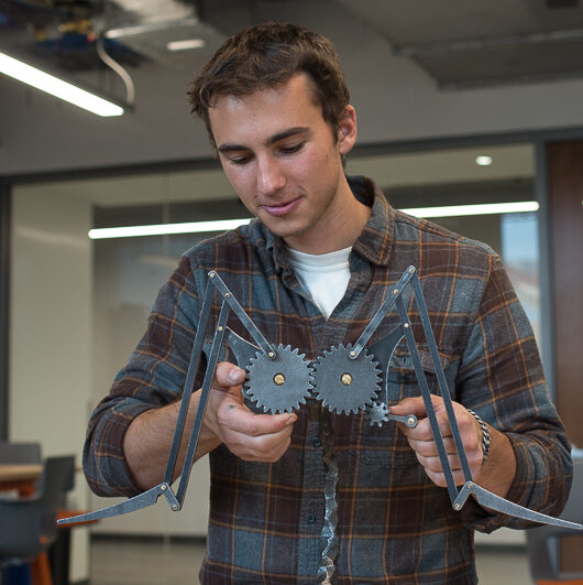 A geotechnical engineer taking a reading with a long yellow device. He is in a white hardhat and orange safety vest.